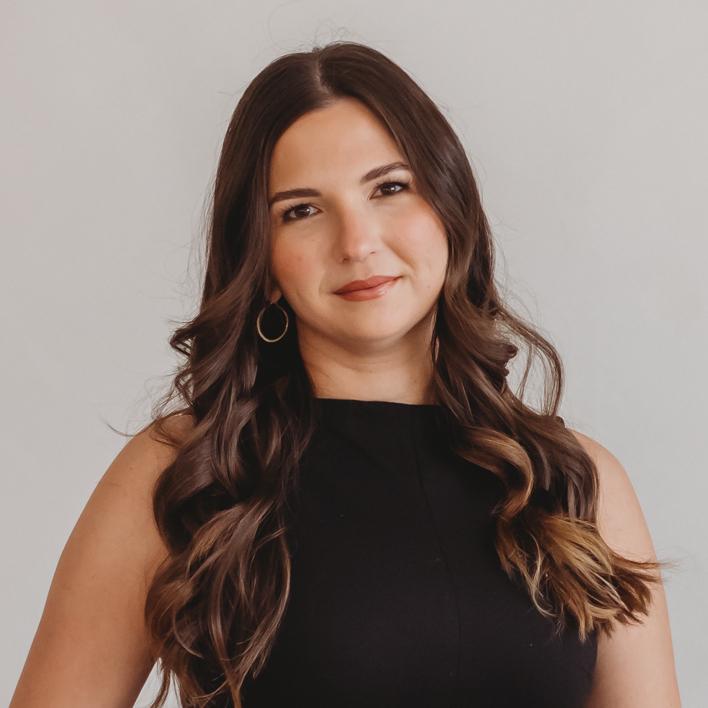 Maggie McTavish with long brown hair wearing a black top against a light background