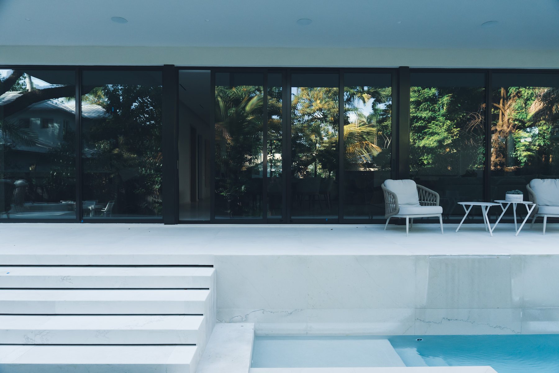 Pool terrace set against broad glass walls and tropical planting