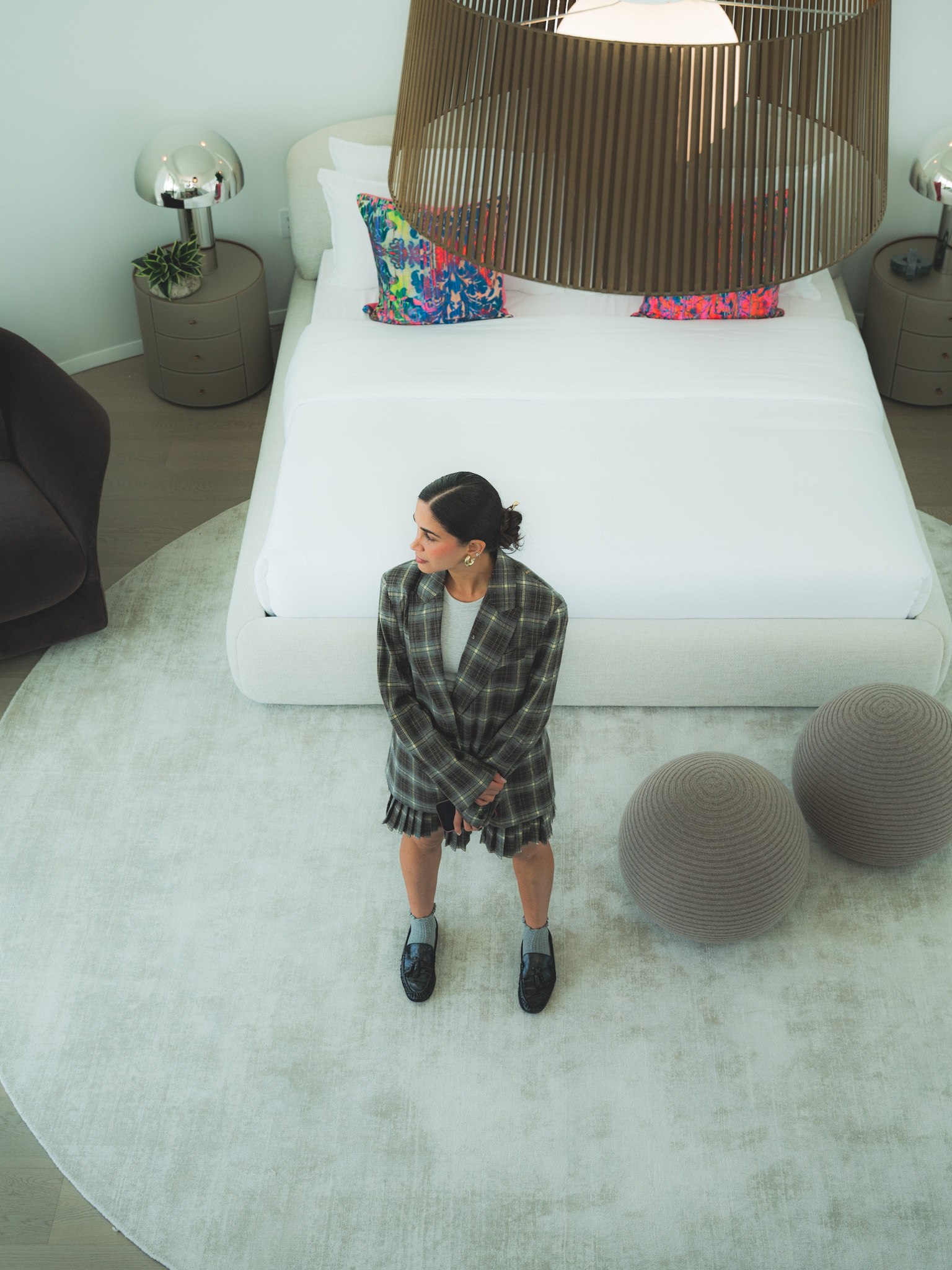 Woman standing in a pale bedroom beneath a sculptural pendant light